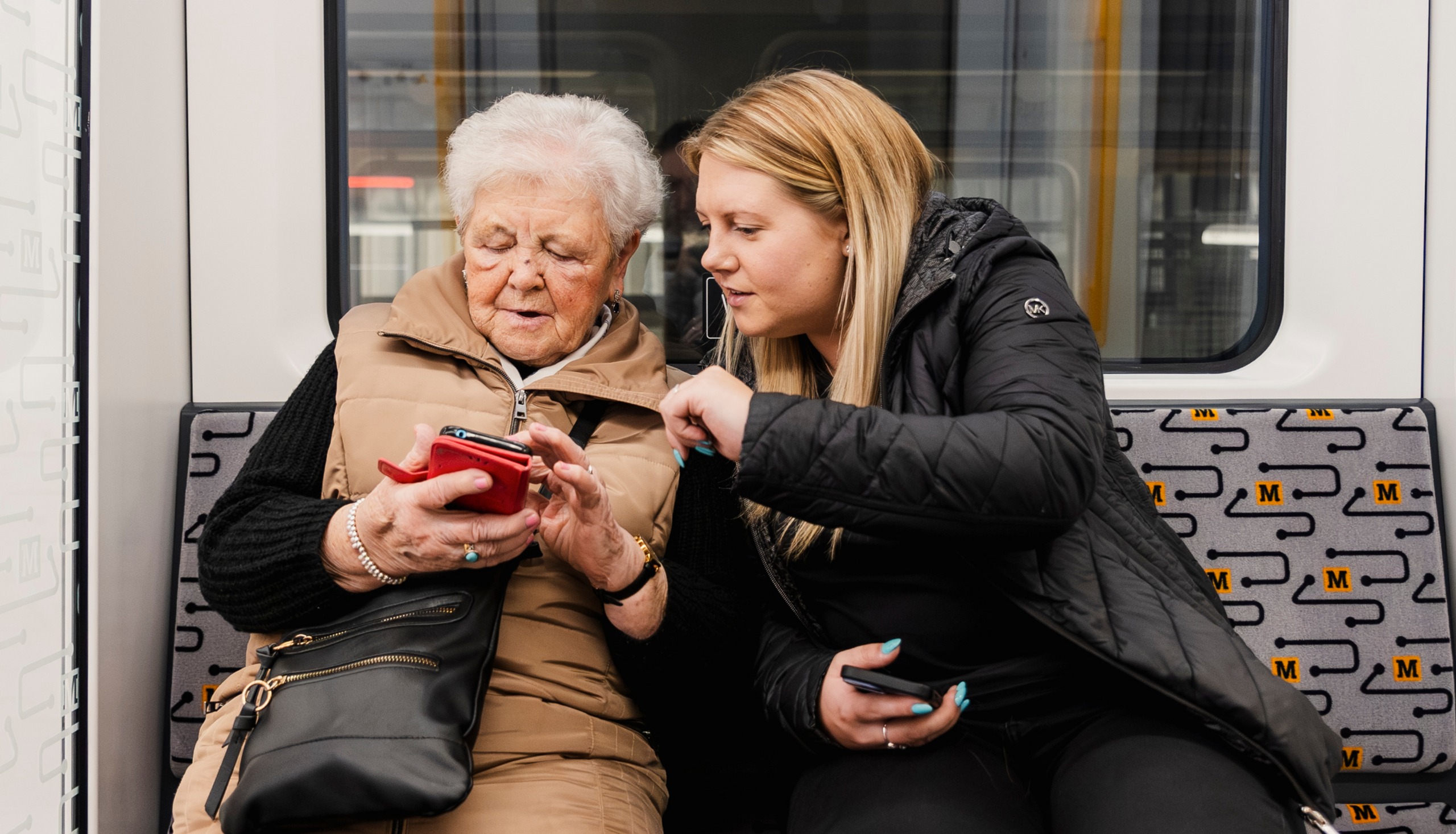 Elderly lady using phone helped by young lady