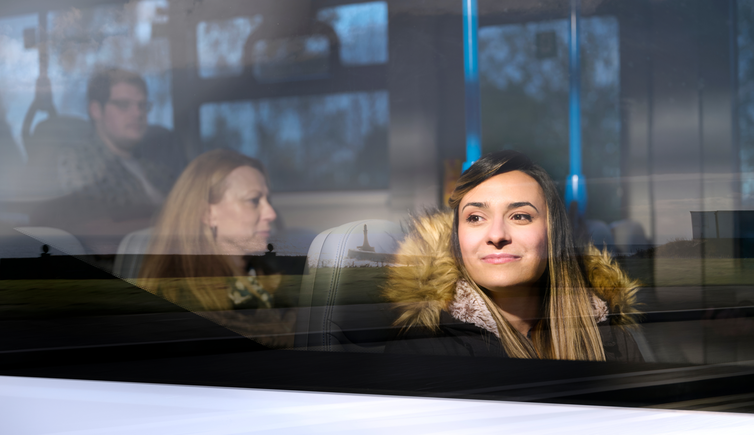 Young woman on bus stares out of window smiling